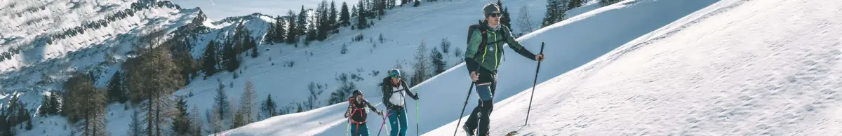 Drei Skitourengeher steigen hintereinander einen verschneiten Hang hinauf