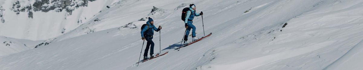 Zwei Personen mit Rucksack steigen auf Tourenski einen verschneiten Hang hinauf