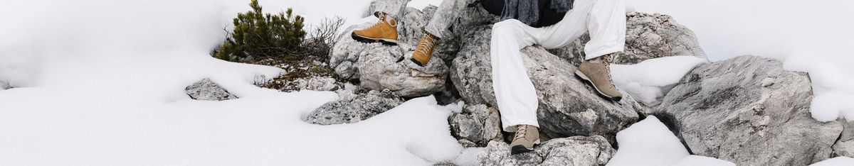 Zwei Personen in Dolomite-Schuhen sitzen auf verschneiten Kalkfelsen