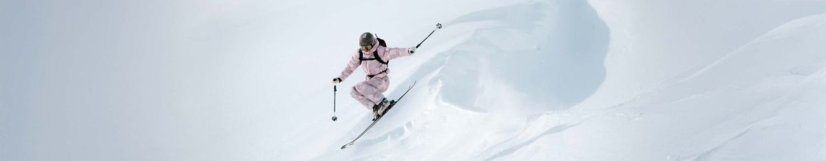 Skifahrerin in rosa Skijacke und Skihose fährt einen verschneiten Hang im Tiefschnee hinab