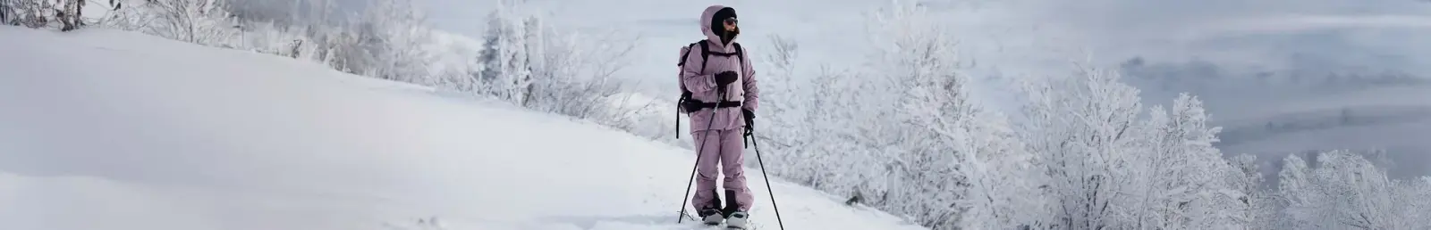 Person in rosa Skitourenkleidung mit Stöcken auf einem verschneiten Hang mit Raureif-Bäumen