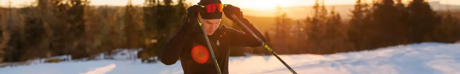 Mann mit LEKI-Skistöcken auf einem verschneiten Hang im Gegenlicht der Abendsonne