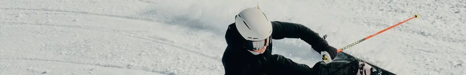Skifahrer mit weißem Uvex-Helm in tiefer Kurve auf präparierter Piste