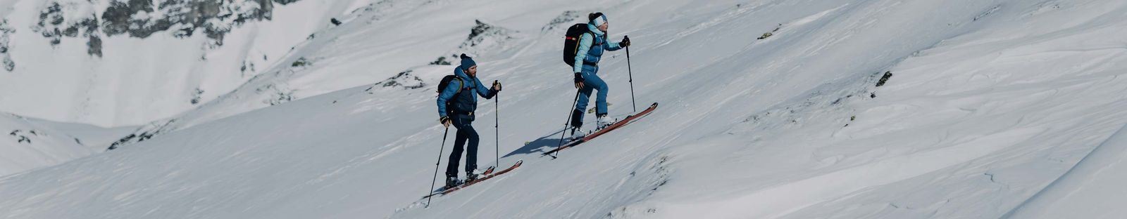Zwei Personen mit Rucksack steigen auf Tourenski einen verschneiten Hang hinauf