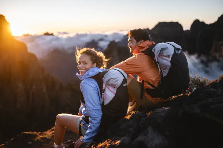 Zwei Wandernde mit Laufrucksäcken sitzen bei Sonnenaufgang auf einem Felsgrat