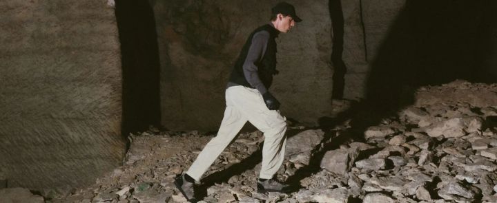 Mann in heller Hose und dunkler Weste steigt in einer Felshöhle über Geröll, an den Füßen Dolomite-Schuhe der 54er-Reihe
