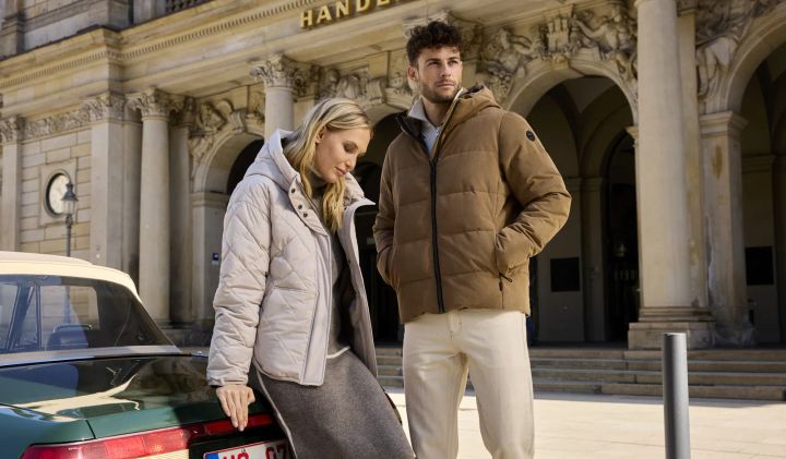Frau in heller und Mann in brauner Steppjacke vor einem historischen Gebäude in der Stadt