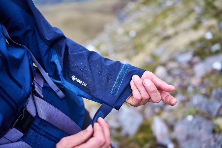 Hand zieht den Klettverschluss am Ärmelbündchen einer blauen Hardshelljacke fest