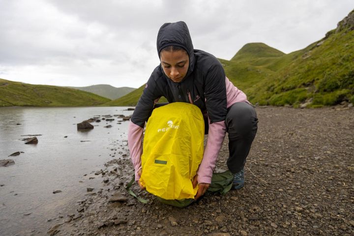 Wanderin zieht am Ufer eines Bergsees eine gelbe Regenhülle über ihren Rucksack