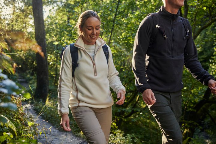 Frau in heller und Mann in schwarzer Fleecejacke wandern mit Rucksack auf einem Waldweg