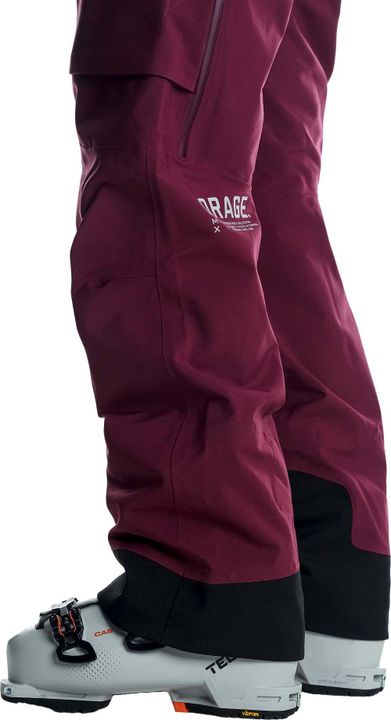 Weinrote Skihose von Orage fällt über weiße Skischuhe, am Saum ein schwarzer Kantenschutz