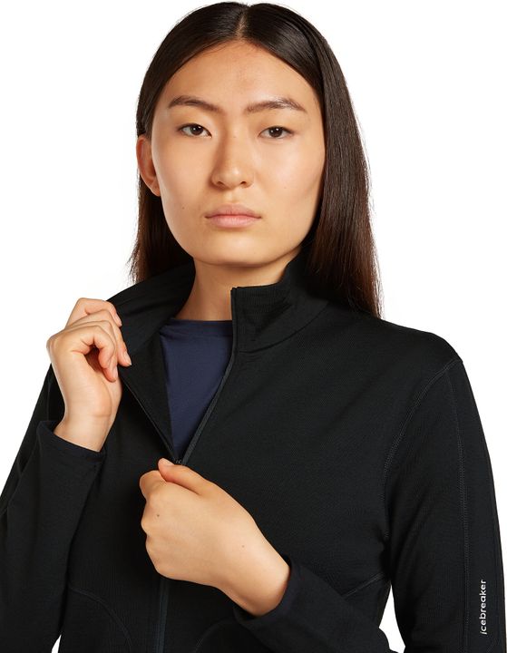 Frau zieht den Reißverschluss einer schwarzen Merino-Fleecejacke hoch