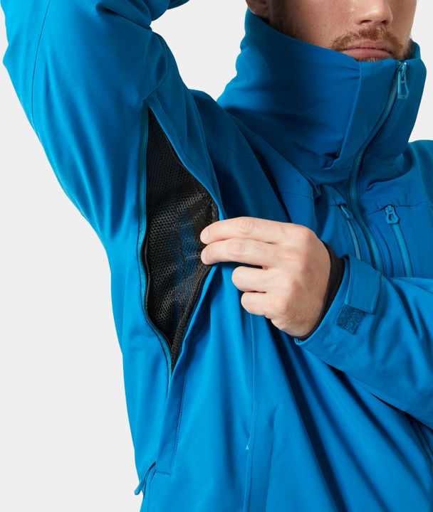 Mann in blauer Helly Hansen Alpha Lifaloft hebt den Arm und öffnet den Belüftungsreißverschluss unter dem Arm