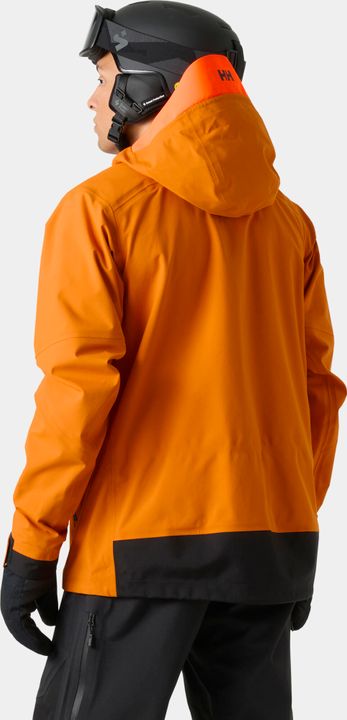 Hand öffnet an einer orangefarbenen Helly-Hansen-Skijacke den Belüftungsreißverschluss unter dem Arm