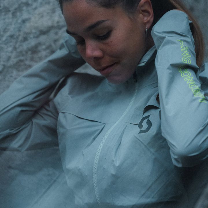 Läuferin in hellblauer Laufjacke mit Kapuze greift an den Kragen