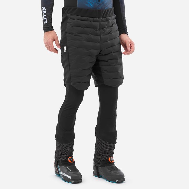 Person in schwarzen, gesteppten Isolationsshorts von Millet über einer schwarzen Tourenhose, dazu Skitourenschuhe