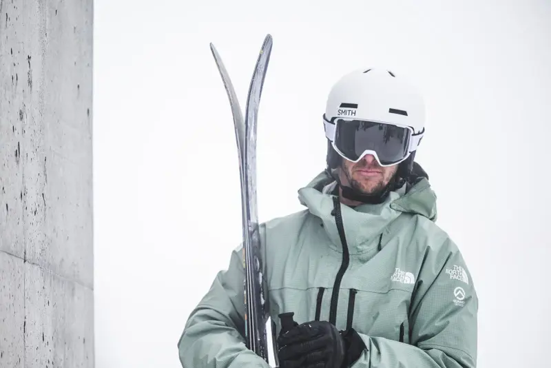 Skifahrer mit weißem Helm und Skibrille, die Ski in den Händen