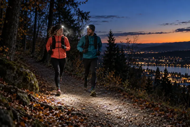 Zwei Läuferinnen und Läufer mit Stirnlampen auf einem Waldweg zur blauen Stunde